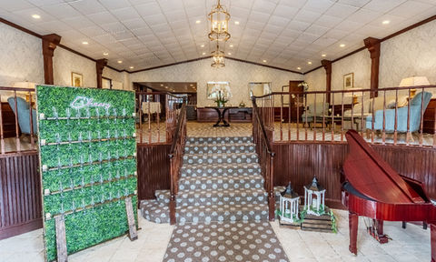 Interior of the Essex Club lobby showing a central staircase with patterned carpet, a green champagne display labeled 'Cheers', and seating areas on either side.