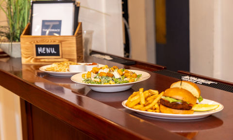 Assorted lunch dishes including Caesar salad, fries with dipping sauces, and a sandwich with fries, displayed on a polished wooden bar.