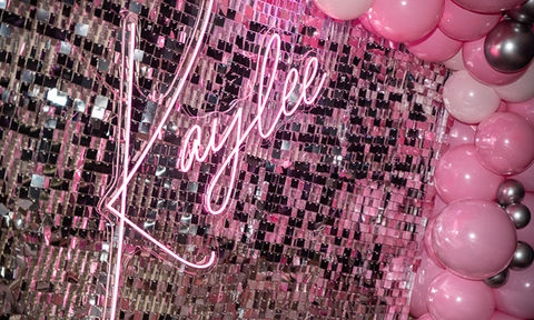 Shimmering silver sequin backdrop featuring a pink neon "Kaylee" sign framed by pink and silver balloons.