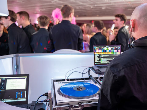 Close-up of a DJ at a mixing booth with a blue vinyl record and laptop during a crowded event.