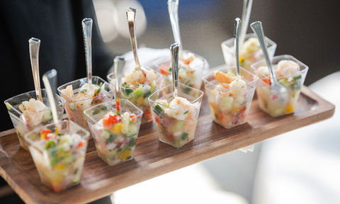 Wooden tray with individual shrimp ceviche cups, each served with a small fork and filled with colorful diced vegetables.