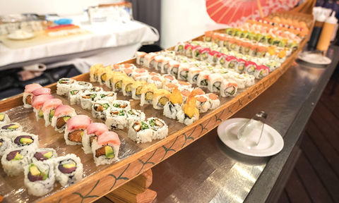 A long wooden boat platter filled with a large variety of colorful sushi rolls.