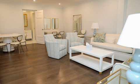Elegant lounge with a white couch, two light blue swivel chairs, a white coffee table, and access to a vanity area through an open door.