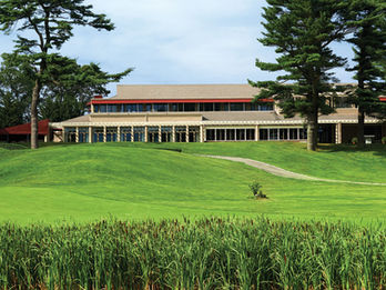 Distant view of the wedding venue building surrounded by trees, seen from across a green lawn and marsh grasses.