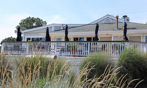 Single-story building with a rooftop deck and closed black umbrellas, viewed from behind tall ornamental grass.