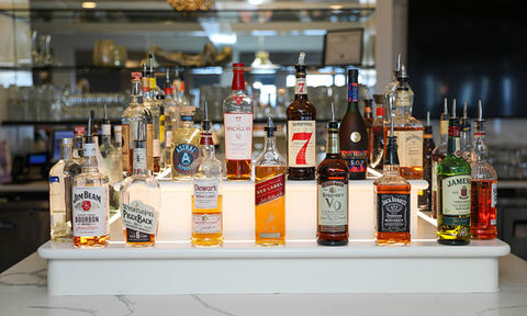 Selection of liquor bottles arranged on a tiered white bar counter in a well-lit lounge area.