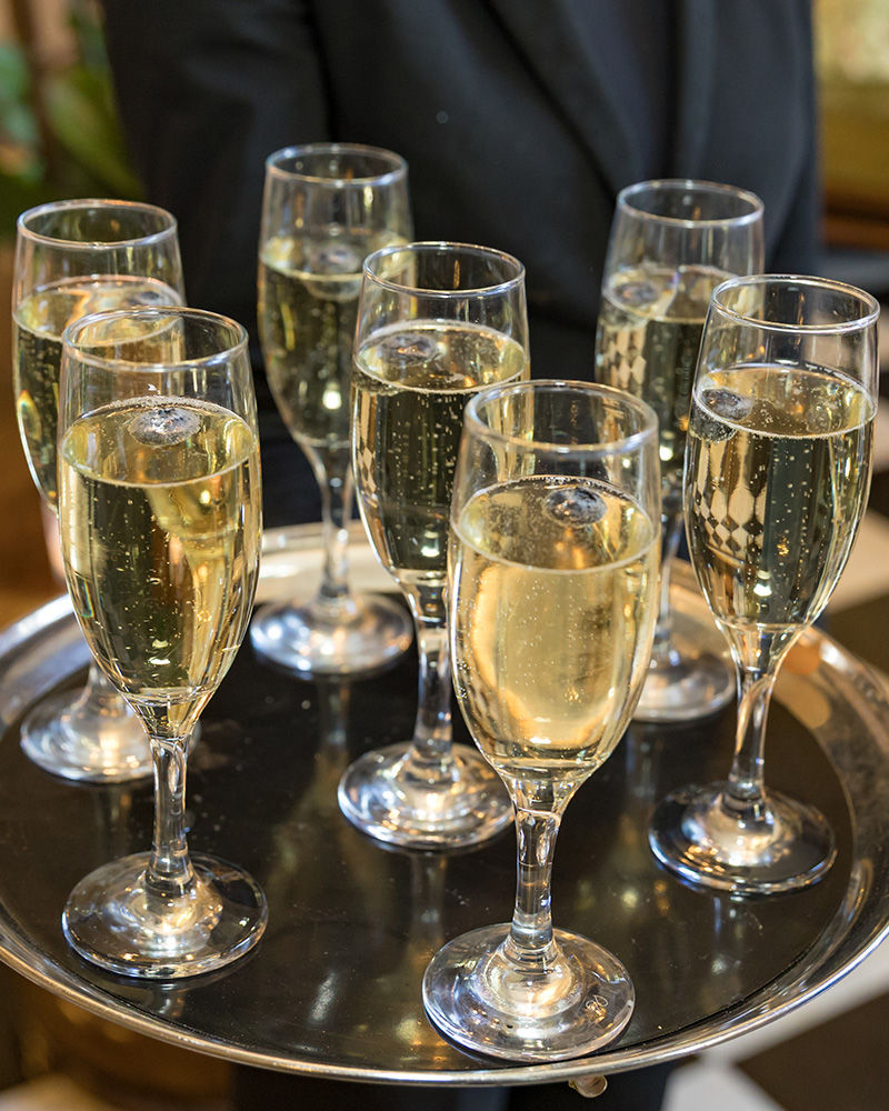 A close-up view of six filled champagne flutes with bubbles, presented on a round silver serving tray.
