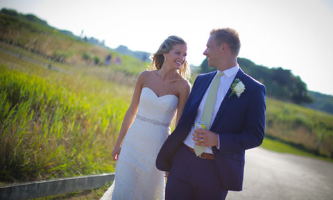 Bride and groom smiling as they walk together along a scenic path surrounded by greenery.