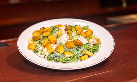 Classic Caesar salad topped with grilled chicken and golden croutons, served in a white rimmed bowl.