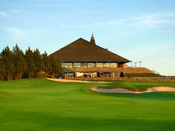 Golf clubhouse with a unique pyramid-style roof, seen from the green with sand bunkers and trees under golden evening light.