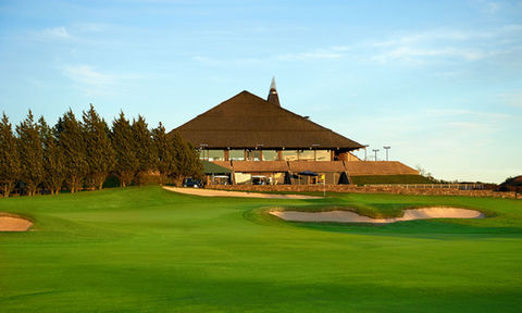Golf clubhouse with a unique pyramid-style roof, seen from the green with sand bunkers and trees under golden evening light.