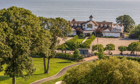 Wide view of a large waterfront property surrounded by trees and a golf course, with the ocean stretching across the background.