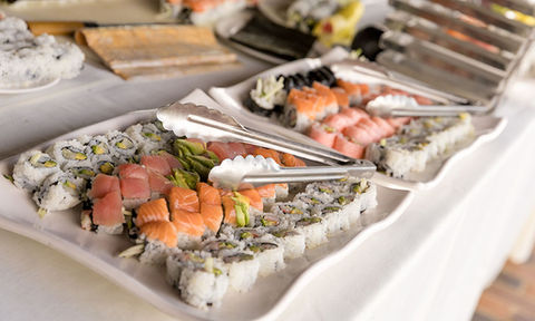 Assorted sushi rolls with raw salmon and vegetables arranged on a white platter with tongs.