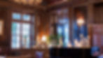 Warmly lit, dark wood-paneled room featuring a black grand piano with glowing candles and large windows in the background.