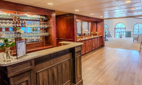 Dark wood bar with glassware, liquor bottles, and a mirrored shelf, located off the main reception area.