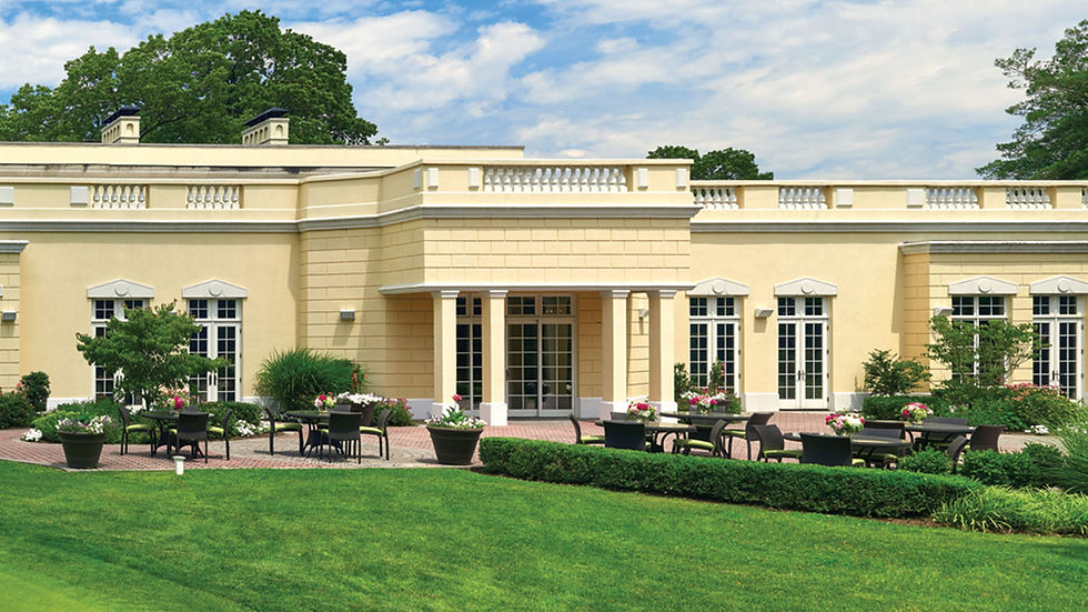 Exterior view of a yellow historic mansion wedding venue with green shutters, a stone fountain, and manicured trees in the courtyard.
