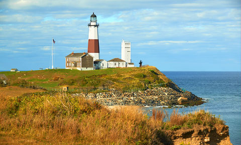 Iconic lighthouse perched on a grassy cliff overlooking the ocean with a rocky shoreline below.