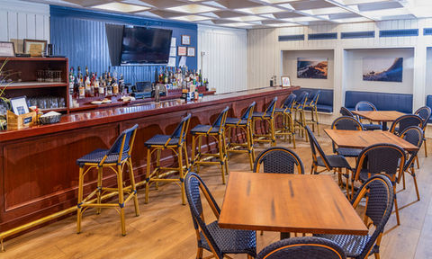 Full service bar with high-top stools, a mounted TV, and an array of spirits, set in a cozy, coastal themed dining space.