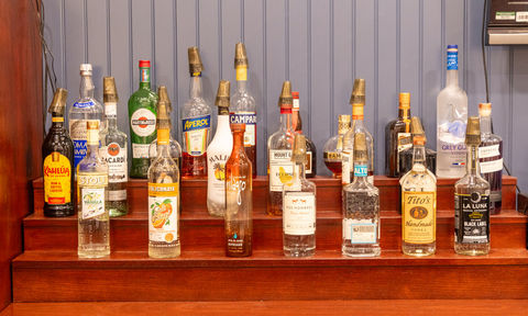 Variety of liquor bottles arranged on a tiered wooden shelf, featuring popular brands like Grey Goose, Tito’s, and Kahlúa.