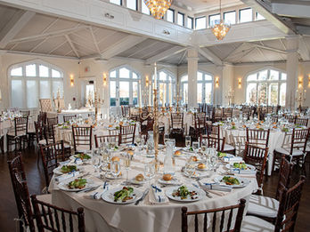 Elegant wedding reception room with white walls, wood floors, and round tables set with plated salads and gold candelabras.