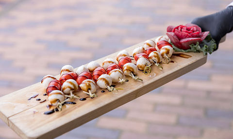 Close-up of a wooden tray with caprese skewers made of mozzarella, cherry tomatoes, and basil, drizzled with balsamic glaze.
