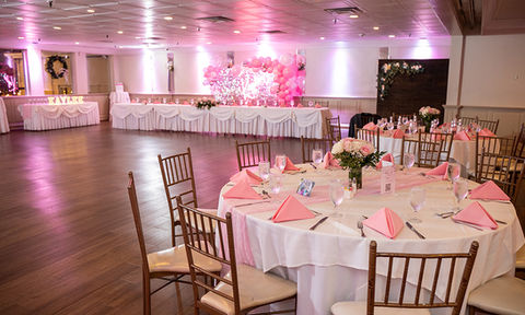 Elegant ballroom featuring round tables with pink accents, floral centerpieces, and a large wooden dance floor.