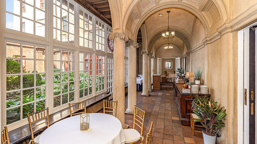 Sunlit hallway gallery with stone arches, large windows, tiled floors, and a small dining setup.