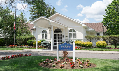 Front entrance of the Essex Club with a white building, covered walkway, manicured landscaping, and a blue sign reading 'Essex Club'.