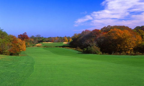 Golf course fairway lined with vibrant autumn trees under a bright blue sky.