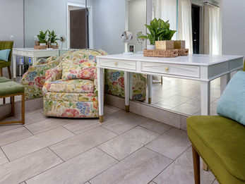 Bridal suite with white vanity tables, floral armchair, and green accent chairs, with full-length mirrors along the wall.