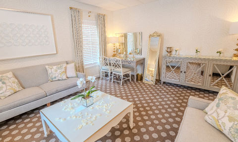 Alternate view of a lounge area showing two sofas, a vanity with mirror, a large leaning mirror, and a white coffee table decorated with flower petals and a small orchid arrangement.