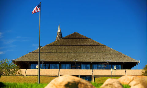 Exterior view of a unique pyramid roof venue with a pointed spire and American flag under a clear blue sky.