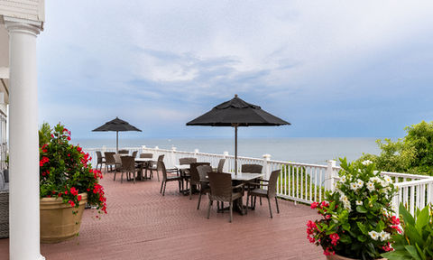 Oceanview patio with black umbrella-covered tables and chairs, surrounded by flower planters and a white railing.
