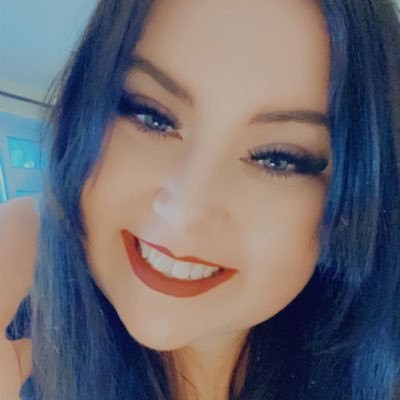 Carly wears red lipstick as she smiles to the camera, taking a selfie. 