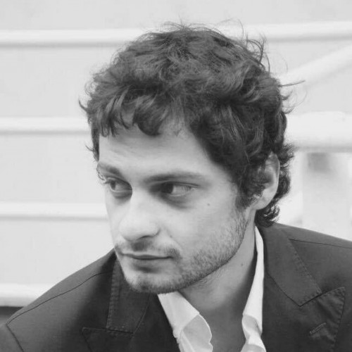 Edoardo is wearing a white shirt and black blazer. He looks over to the left of the camera.