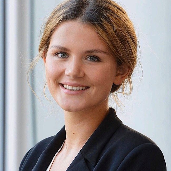 Alexia wears a black blazer as she smiles to the camera.