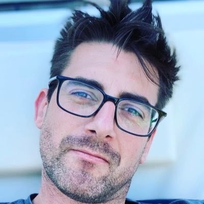 Jordan wears black framed glasses as he looks to the camera calmly