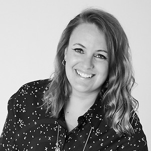 Harriet smiles to the camera infront of a white background. She wears a black blouse with a starry pattern.
