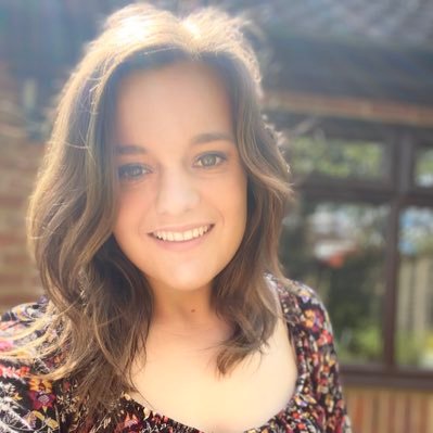 Katie smiles to the camera in her garden while wearing a floral dress.