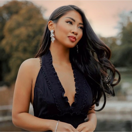 Brooklyn stands outdoors with trees in the background. She wears a black halterneck dress as she looks over to the right. Her hair blows in the breeze.