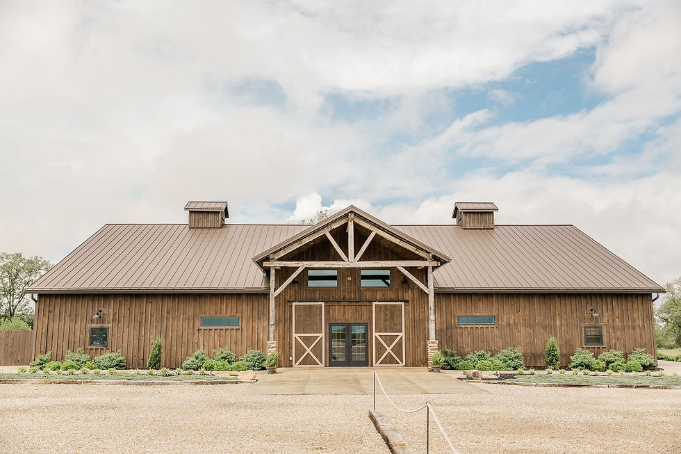 Central Ohio Wedding Venue Rustic barn-style wooden building with brown metal roof and gravel drive under a bright cloudy blue sky.