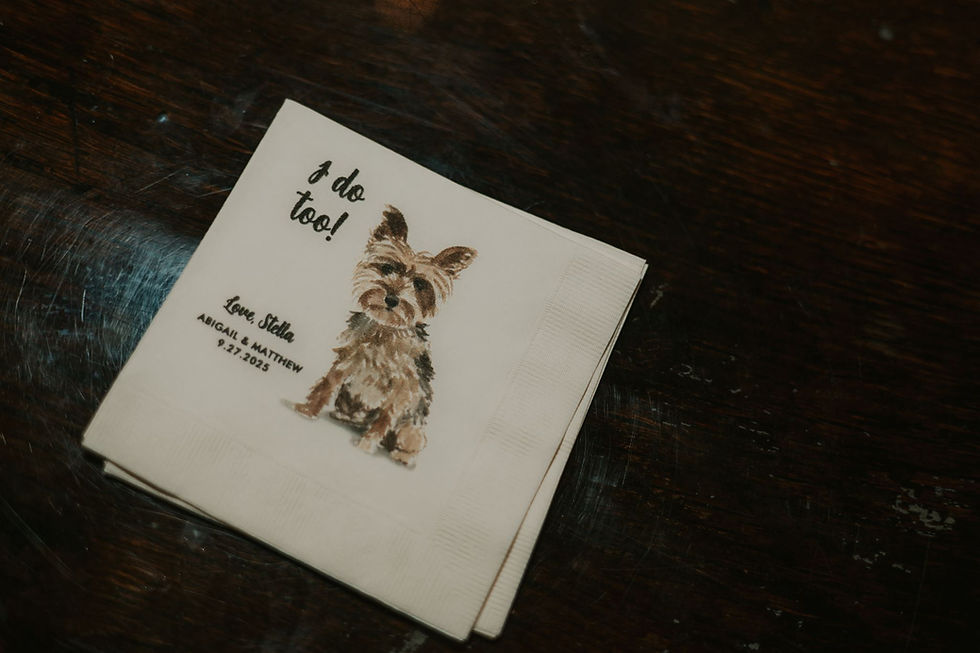 Rustic Columbus wedding venues Napkin with a dog illustration and text "I do too! Love, Stella" on a wooden table. Wedding date: 9.27.2025. Casual, warm setting.