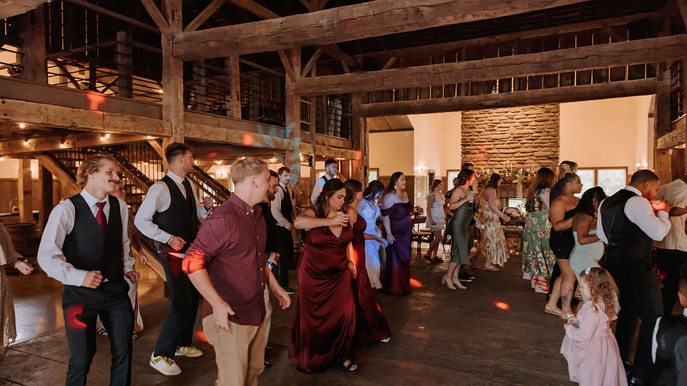 wedding venue Ohio People in formal attire dancing in a rustic hall with wooden beams and a stone wall. Warm lighting and festive mood.