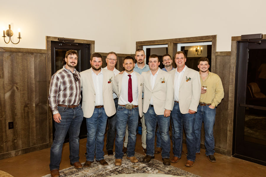 Barn Wedding Venues in Ohio. Eight men in casual and formal attire pose together indoors. The setting features wooden walls and warm lighting, creating a cozy atmosphere.
