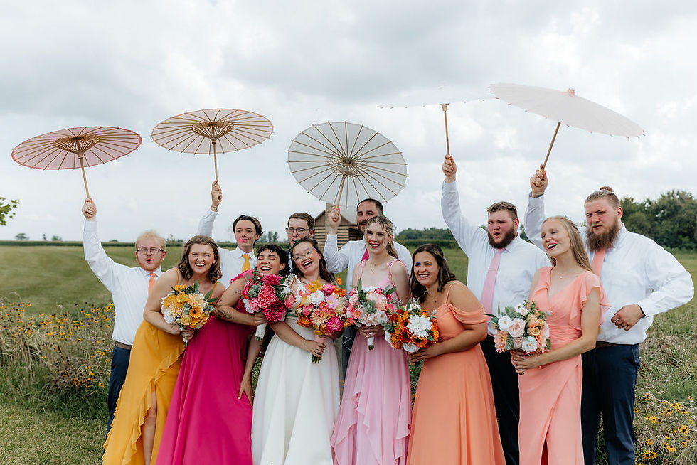 Columbus Wedding Venue Smiling wedding party outdoors in a field, women in bright dresses and men in white shirts holding parasols and bouquets