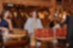 Wedding Experience Ideas Ohio Venue. Women in a rustic hall are at a buffet table with skewered meat. Warm lighting, wood beams, and stairs in the background. Casual atmosphere.