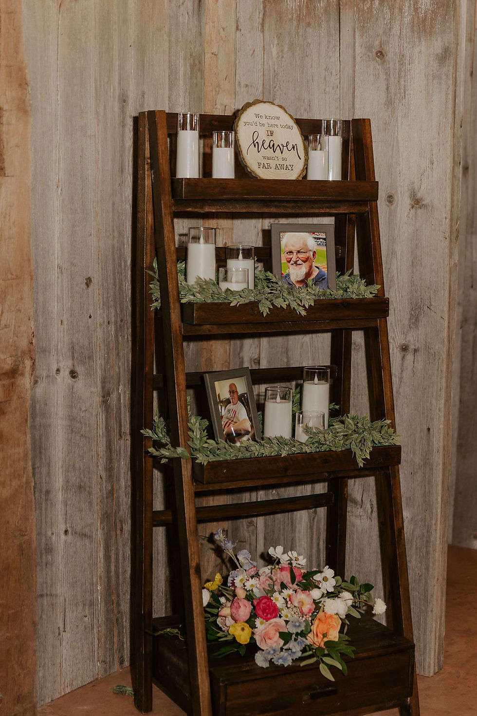 Wedding Experience Ideas Ohio Venue. Wooden shelf with candles, framed photos, and a sign reading "We know you'd be here today if heaven wasn't so far away." Floral arrangement below.
