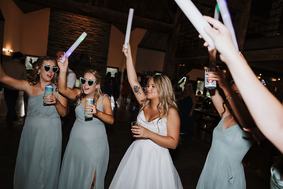 Central Ohio Wedding Venue Bridesmaids and bride in light blue and white dresses dance with glow sticks and drinks at a rustic indoor wedding reception.