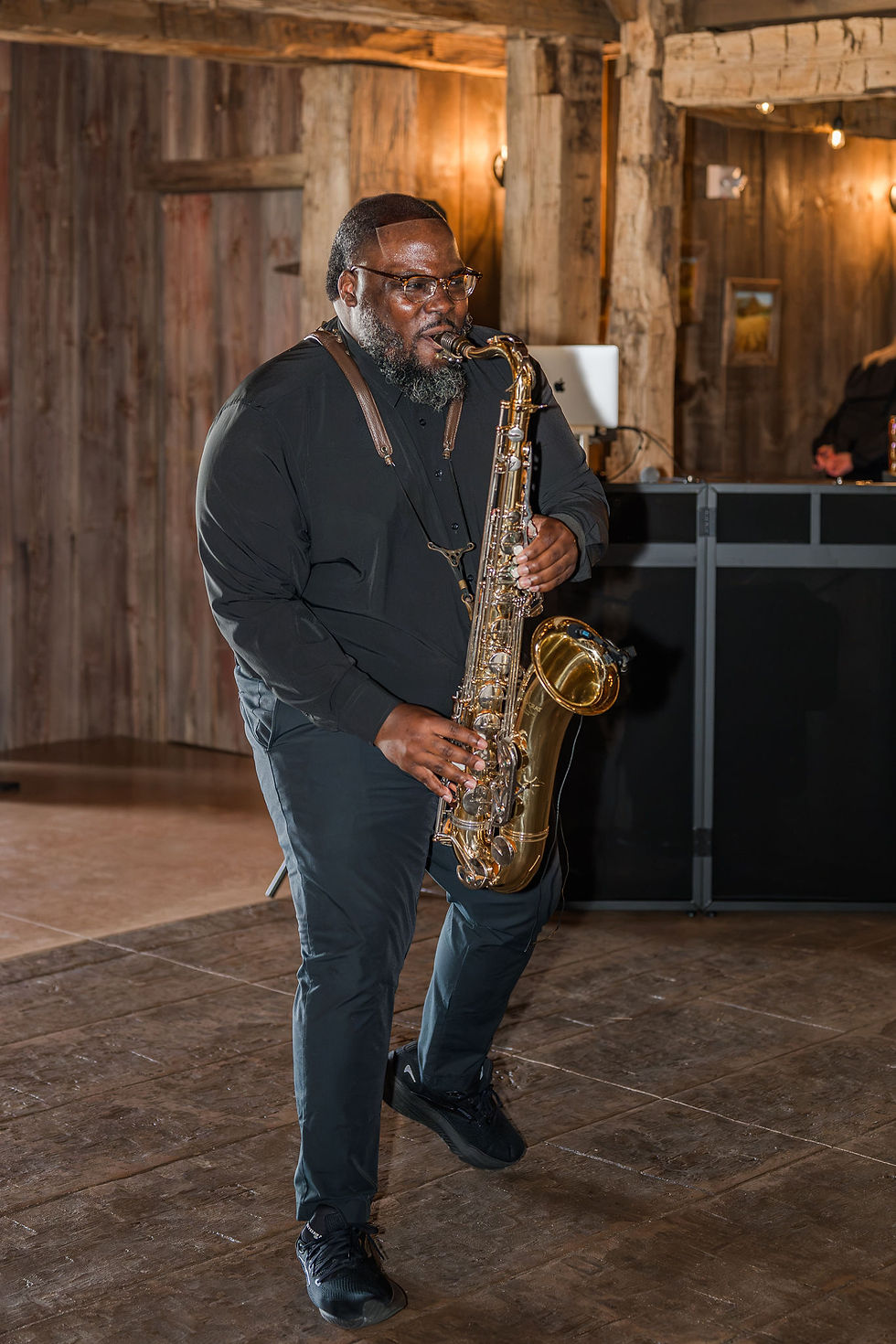 Pickaway County Wedding Venue Black-clad saxophonist performing in a rustic wood-paneled venue, focused and mid-step under warm lights.
