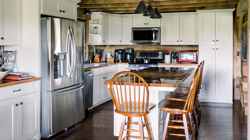 Ohio Wedding Venue. Rustic kitchen with white cabinets, stainless steel appliances, and a wooden island with chairs. Warm lighting and wooden beams. Cozy feel.